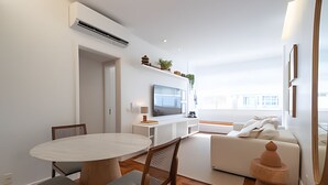 A modern living room with a round dining table, wooden chairs, a white sofa, and a television. - Impeccable apartment in a great location in Leblon (Rio de Janeiro)