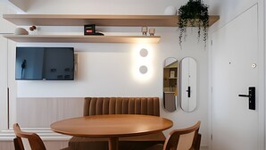 Un comedor moderno con una mesa redonda de madera y cuatro sillas. Sobre la mesa, dos espejos en la pared y un televisor de pantalla plana.