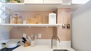Una cocina moderna con armarios blancos, un lavamanos de acero inoxidable y estantes de madera.