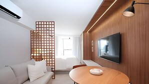 Uma sala de estar moderna com sofá, divisória de madeira, mesa de jantar redonda e televisão de tela plana na parede.