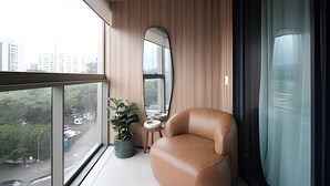 Uma varanda moderna com uma poltrona de couro, uma planta em vaso e vista para a paisagem urbana.