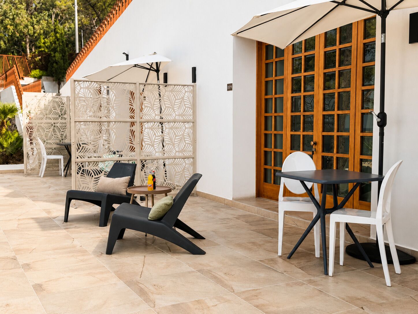 Zona esterna con posti a sedere, tavolo, sedie, un pannello decorativo e una porta in legno con vetri.