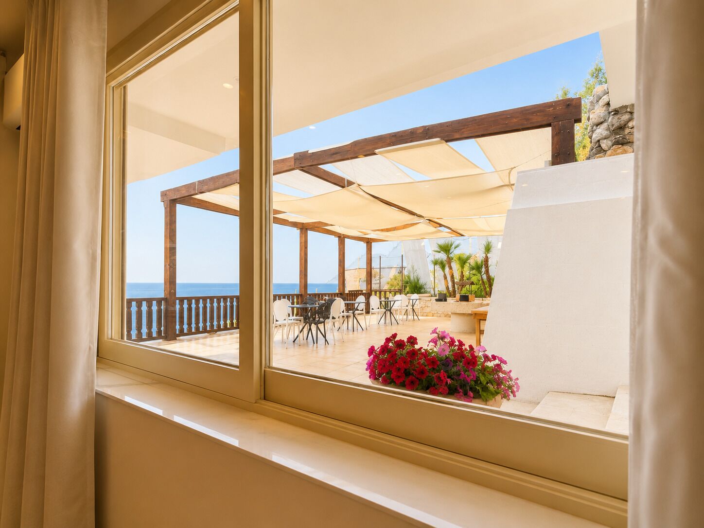 Un balcón con vista al mar, mobiliario exterior y un arreglo floral.
