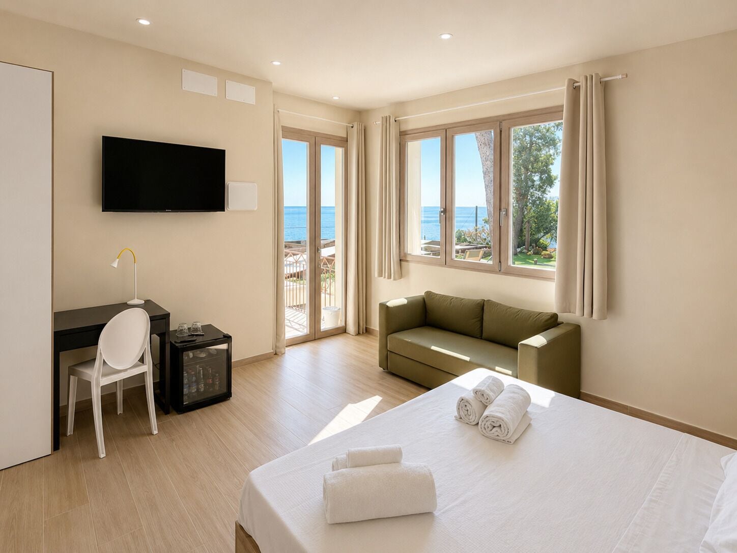 Quarto de hotel com cama, escrivaninha, cadeira, televisão e varanda com vista para o mar.