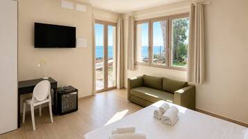 Quarto de hotel com cama, escrivaninha, cadeira, televisão e varanda com vista para o mar.