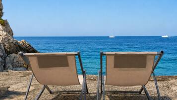 Two beach chairs facing the sea with rocky terrain and a clear sky.