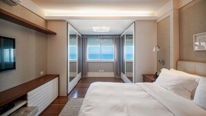 Une chambre d’hôtel moderne dotée d ’un grand lit, d’une télévision, d’une table de chevet et offrant une vue sur la mer grâce à une porte coulissante.