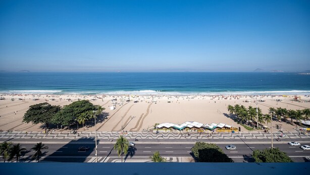 Une plage avec une route au premier plan, des palmiers et un ciel bleu dégagé.