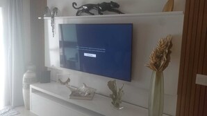 Un téléviseur à écran plat fixé sur un meuble de rangement blanc, agrémenté d’objets décoratifs, notamment une sculpture et un vase.