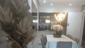 Un espace de salle à manger moderne avec une table et des chaises blanches, un vase de fleurs et un luminaire lumineux.