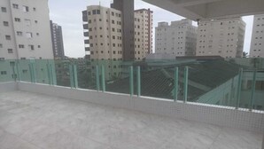 Un balcon spacieux doté d’un sol carrelé et d’une balustrade en verre, offrant une vue sur un paysage urbain avec de nombreux immeubles de grande hauteur.