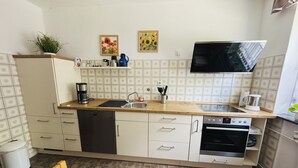 Une cuisine compacte équipée d’un lave-vaisselle, d’un four, d’un évier et d’un téléviseur à écran plat fixé au-dessus du plan de travail.