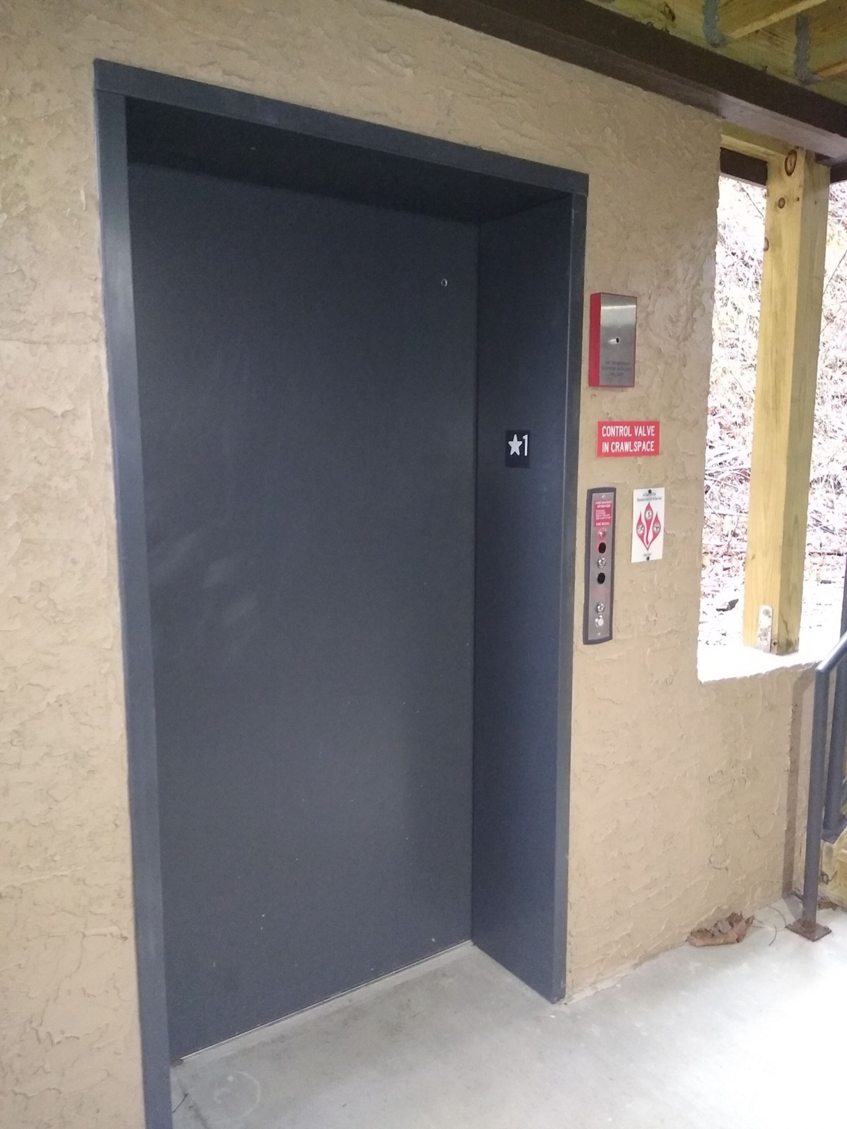 A closed elevator door with a control panel and a warning sign on the wall.