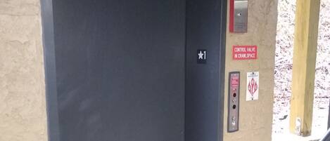 A closed elevator door with a control panel and a warning sign on the wall.