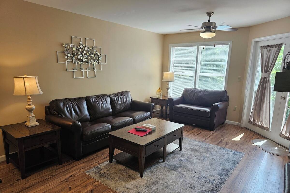 A living room with a brown leather sofa, a wooden coffee table, a decorative wall piece, and a ceiling fan.