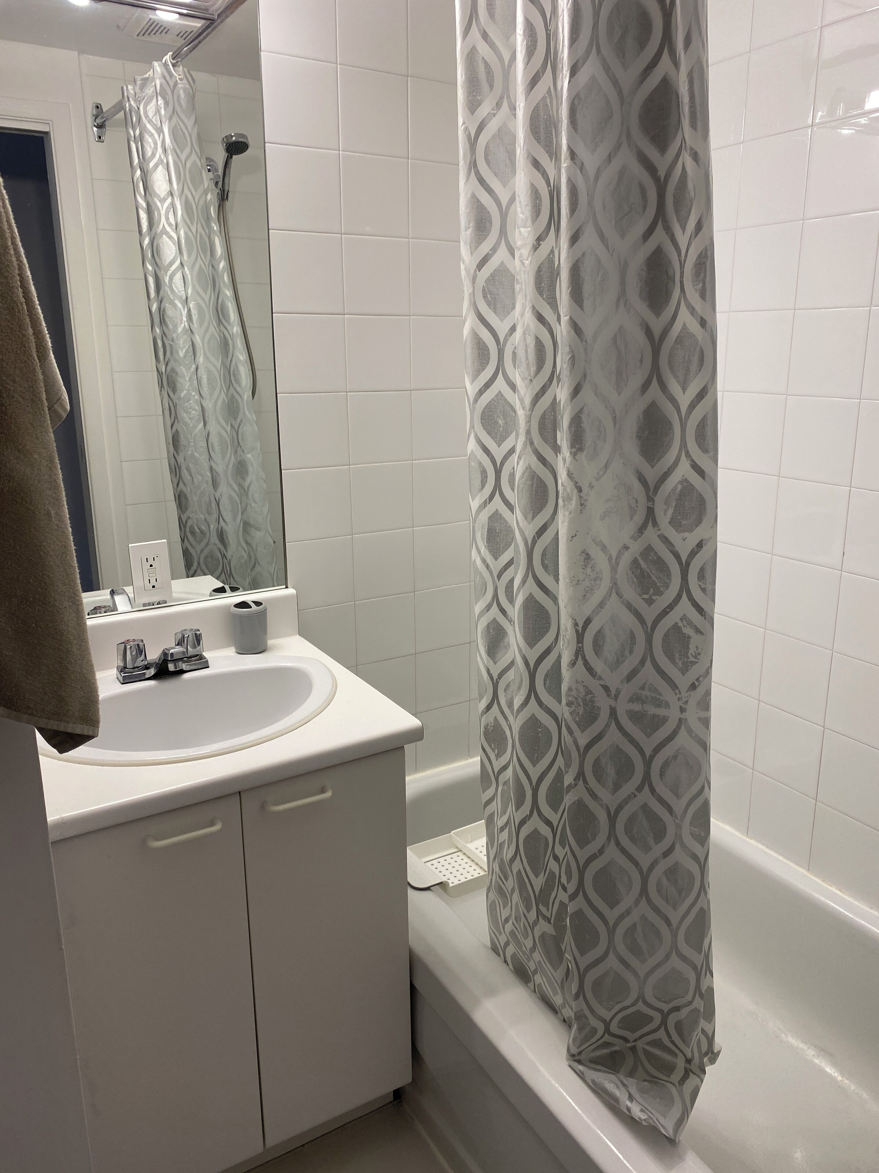 Un baño con lavamanos blanco, espejo y ducha con cortina estampada.