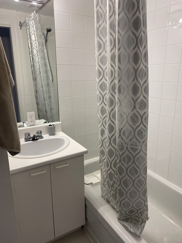 Un baño con lavamanos blanco, espejo y ducha con cortina estampada.