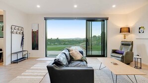Una sala moderna con un amplio ventanal corredera que da a una vista panorámica al exterior, un sofá de cuero, una mesita y una silla.