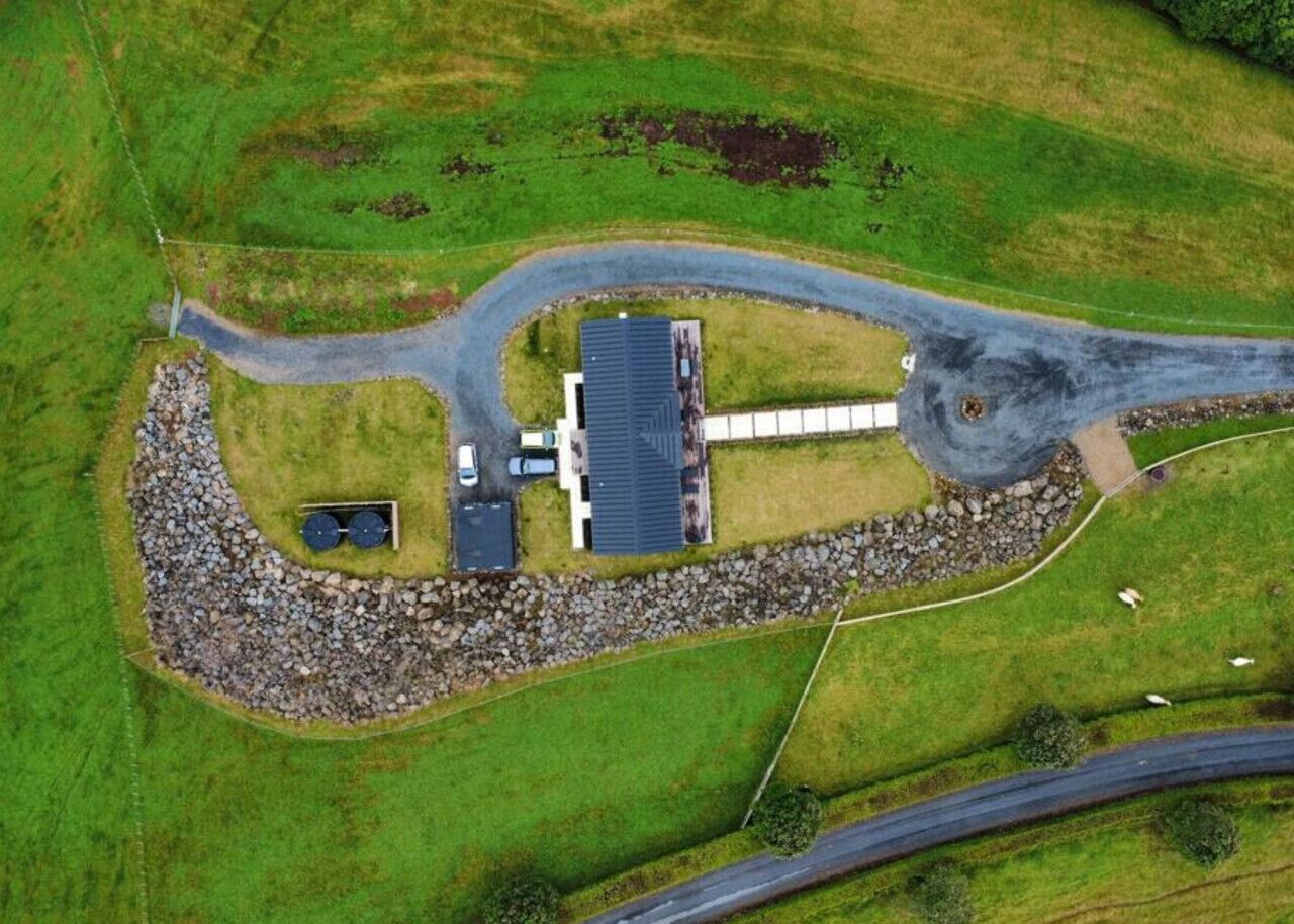 An aerial view of a rural property with a house, a gravel driveway, and a circular stone feature.