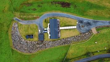 An aerial view of a rural property with a house, a gravel driveway, and a circular stone feature.