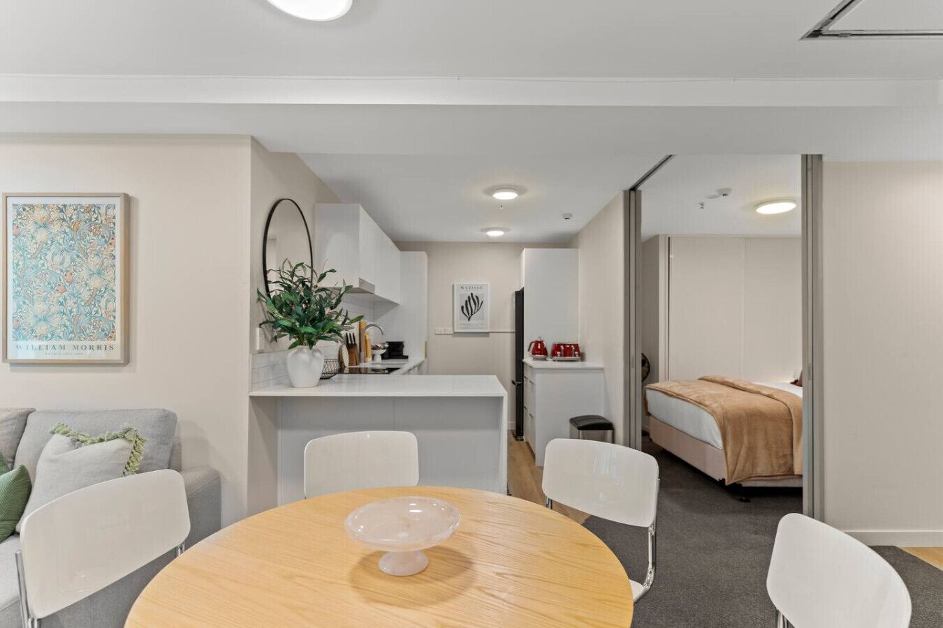 A modern, compact hotel room with a dining area, kitchenette, and a bed.