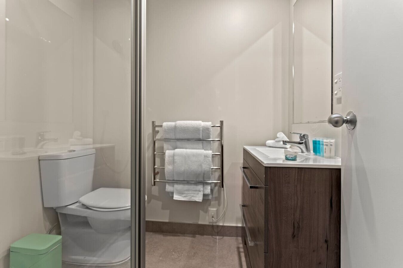 Une salle de bain moderne avec une douche à parois de verre, des toilettes, un lavabo avec des articles de toilette et un porte-serviettes.