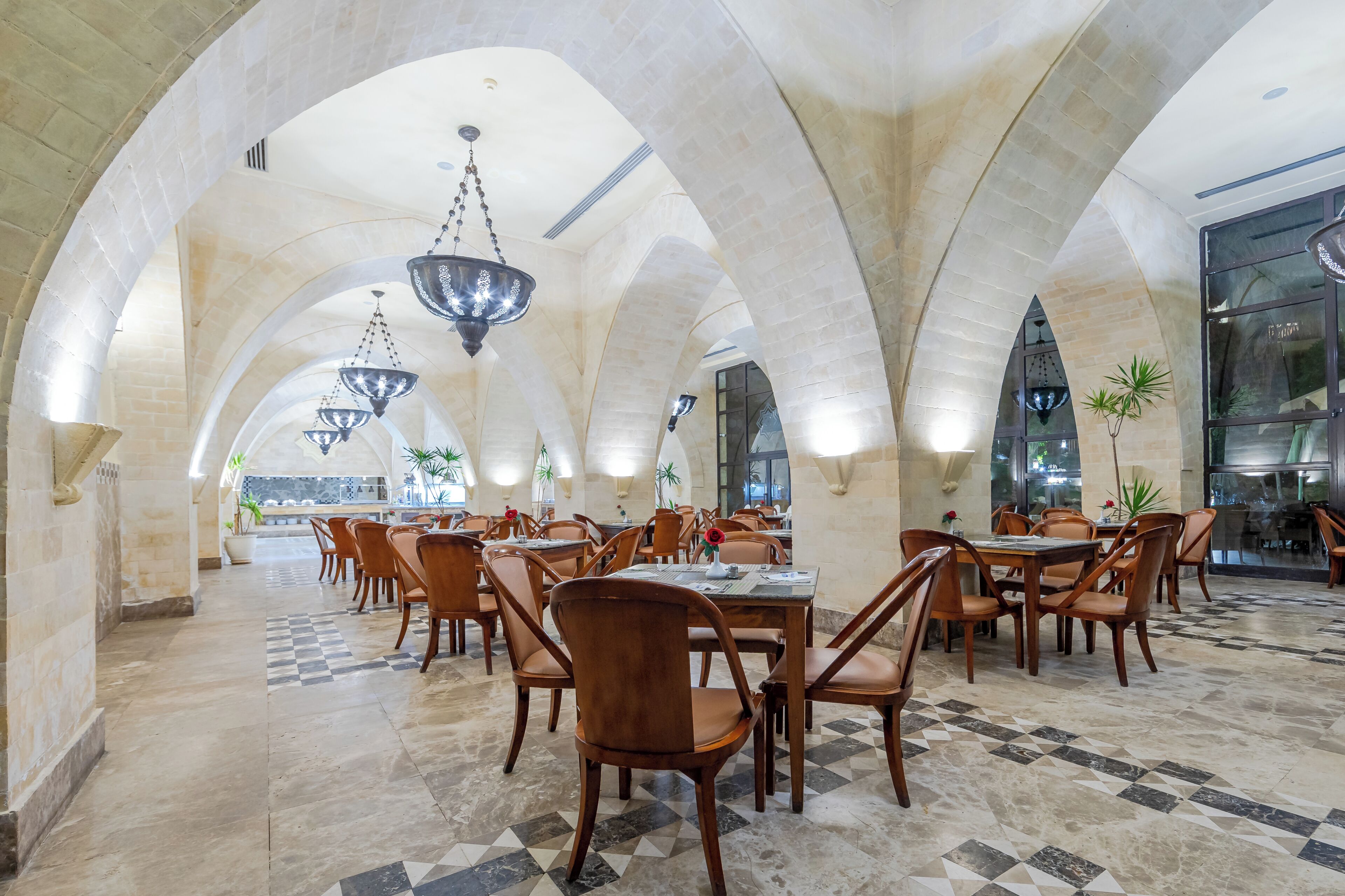 Un comedor amplio con techos altos en arco, varias mesas y sillas, y candelabros colgantes.