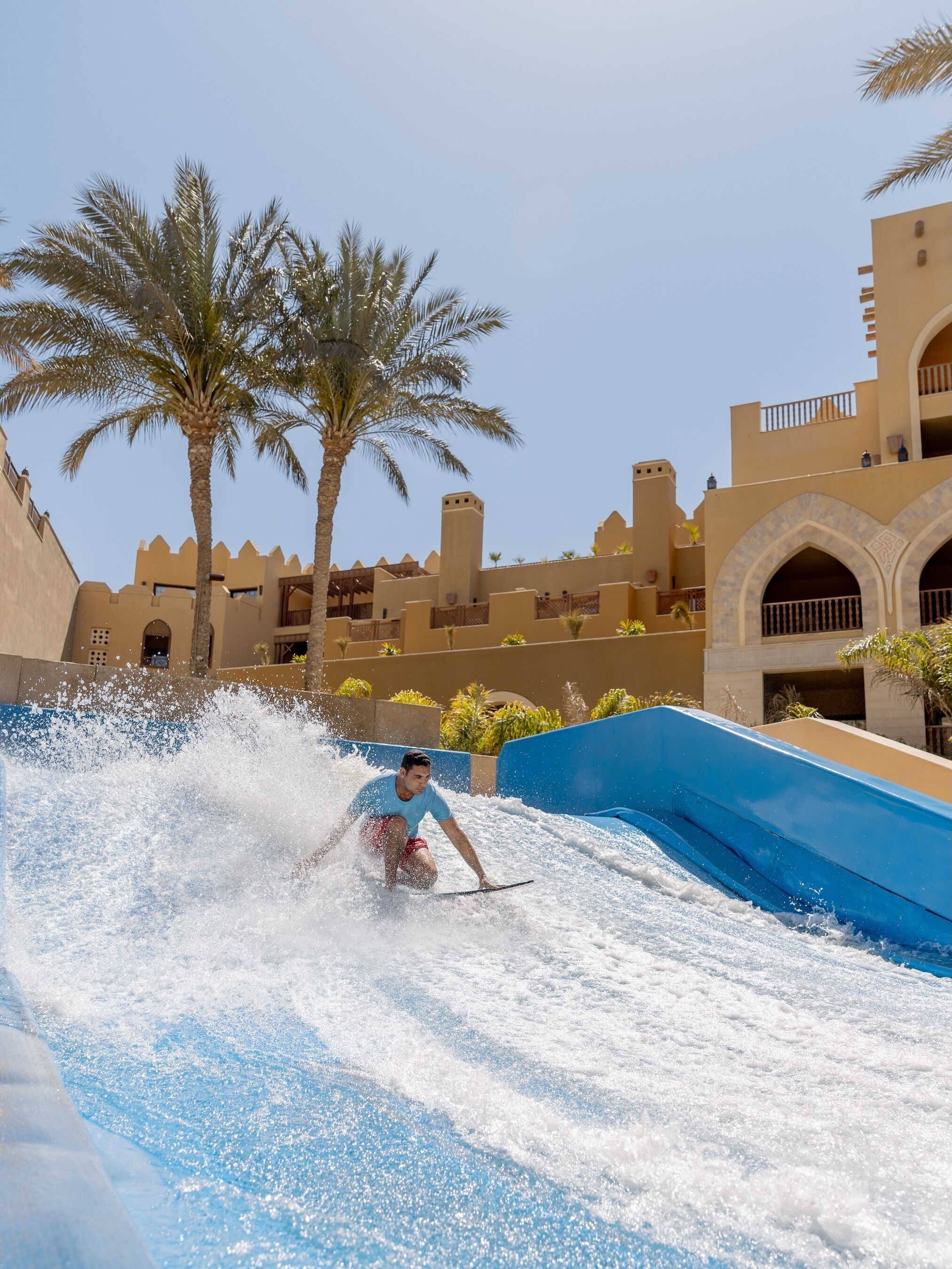 A water slide at a resort with palm trees and traditional architecture in the background.