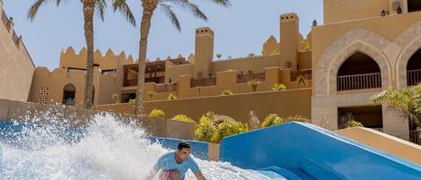 A water slide at a resort with palm trees and traditional architecture in the background.