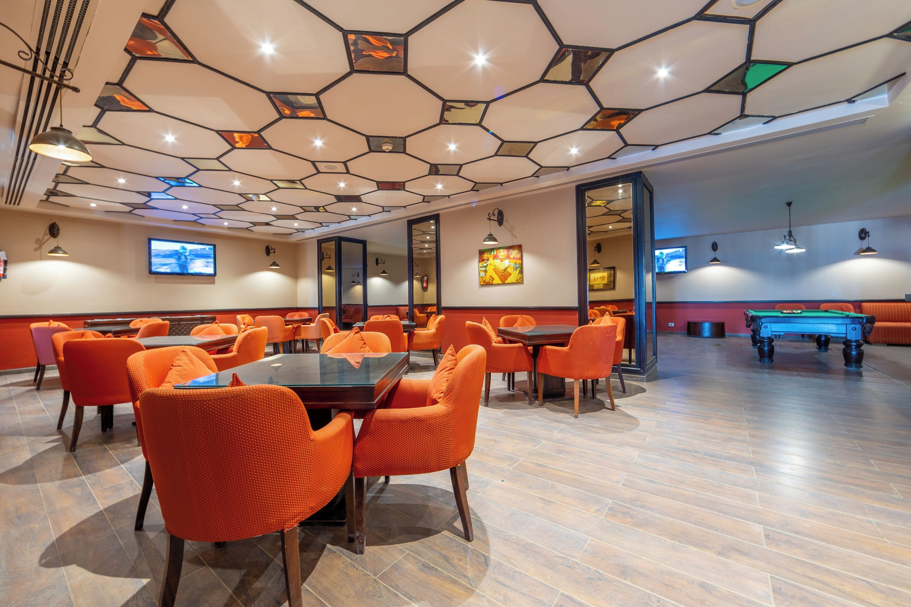 Un comedor moderno con baldosas hexagonales en el techo, sillas anaranjadas y una mesa de billar.