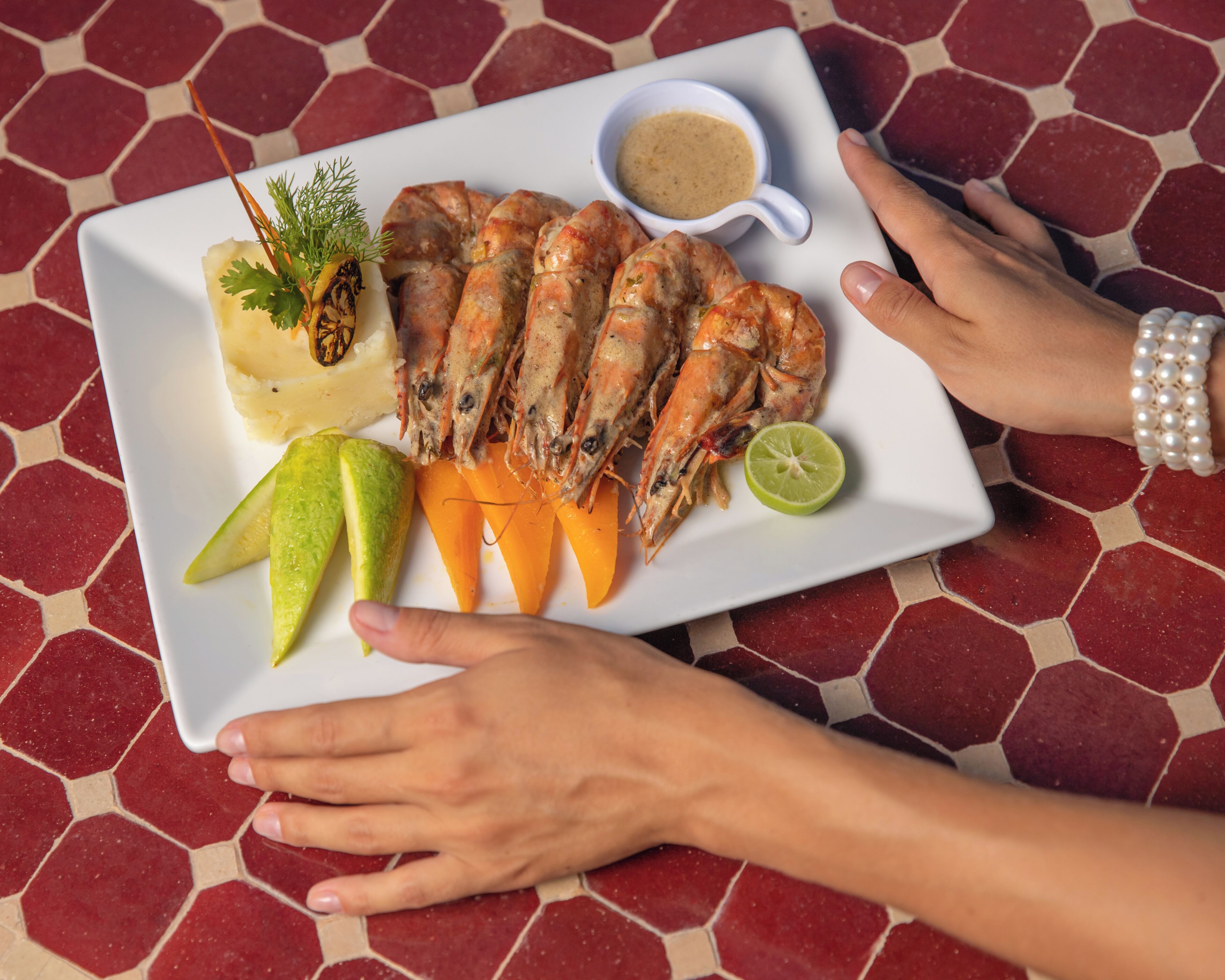 A plate of food with shrimp, carrots, and a lime wedge, accompanied by a small bowl of sauce.