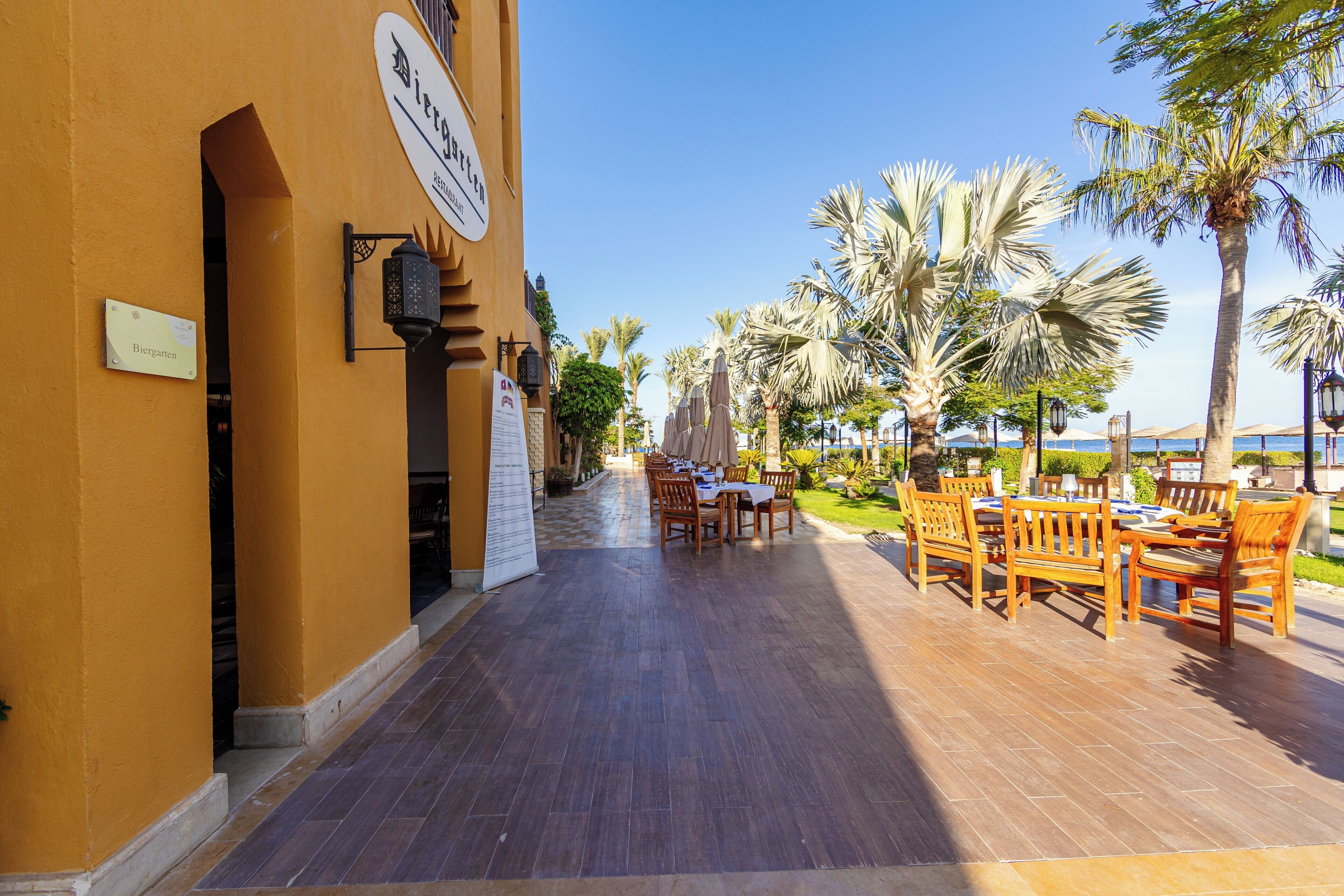 A restaurant with outdoor seating, palm trees, and a clear sky.