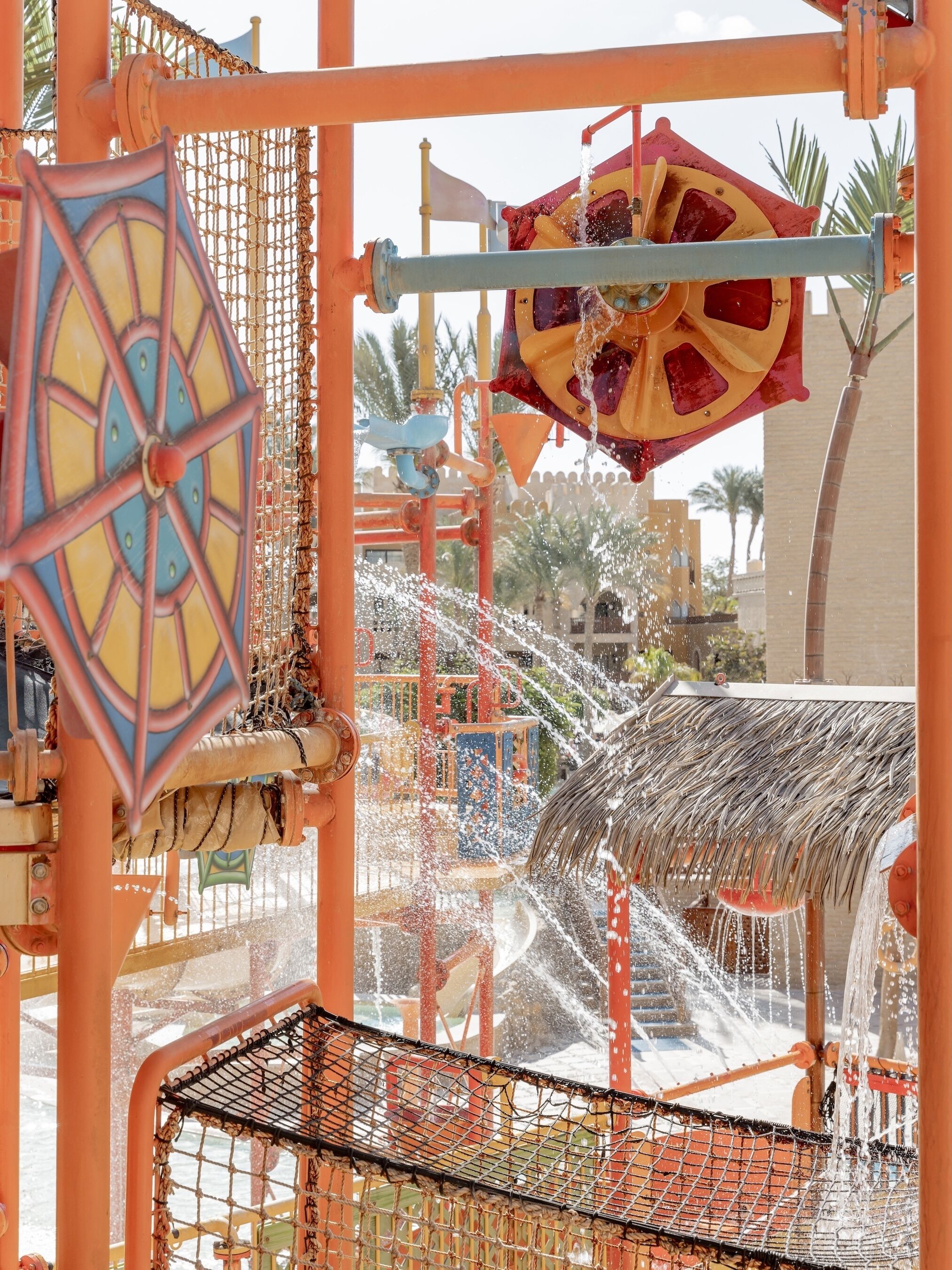 Un parque acuático con toboganes de agua, estructuras de juego cubiertas con malla y una zona de juegos colorida.