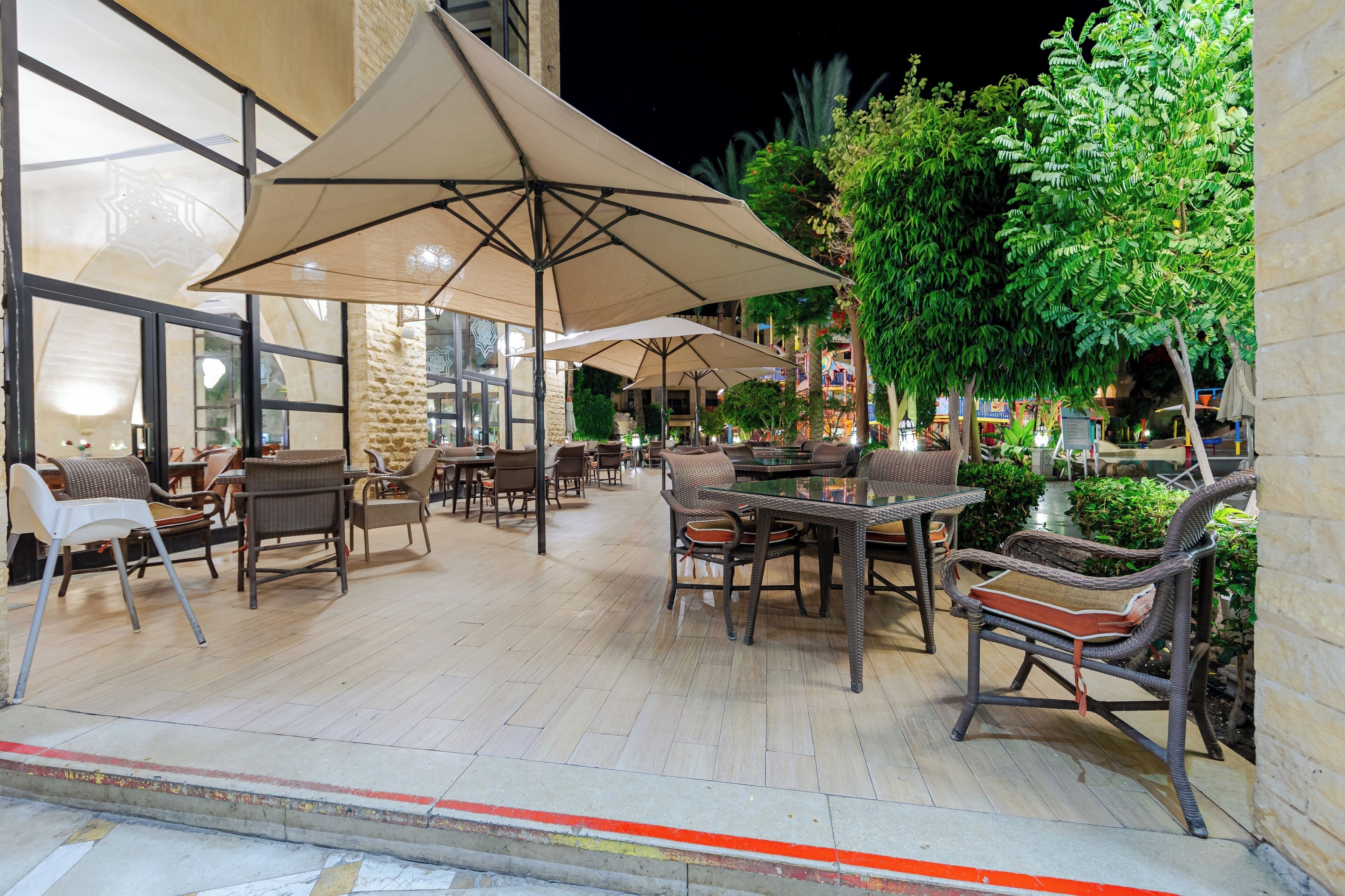 An outdoor seating area with tables and chairs, large umbrellas, and greenery.