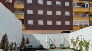 A rectangular swimming pool with clear blue water, surrounded by a paved deck. There are lounge chairs and umbrellas along the poolside. - Casa Ribera Maya (Aranda de Duero)