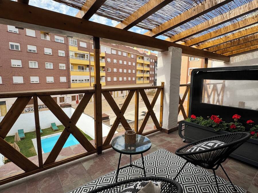 A balcony with a view of a building, a pool, and outdoor furniture.