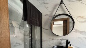 A modern bathroom with a glass-enclosed shower, a black sink with a wooden soap holder, and a round mirror on the wall. - Casa Ribera Maya (Aranda de Duero)
