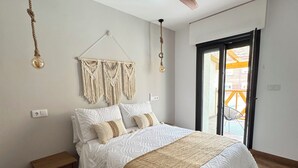 A bedroom with a bed, wooden floor, ceiling fan, macramé wall hanging, and a view through a glass door. - Casa Ribera Maya (Aranda de Duero)