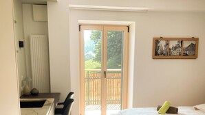 A bedroom with a wooden bed, a desk, and a chair. There is a sliding glass door leading to an outdoor balcony. - Apartment Weißhorn (Barbian)
