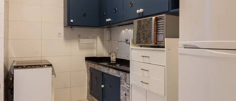 A compact kitchen with white cabinets, a white refrigerator, and a microwave on the countertop.