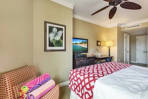 A hotel room with a bed, a desk, a television, a ceiling fan, and a framed picture on the wall.