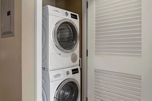 A Bosch washing machine stacked on top of another Bosch washing machine in a laundry room with a white door and blinds.