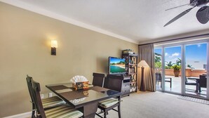A hotel room with a glass dining table, chairs, a television, a bookshelf, a lamp, and a ceiling fan. - Honua Kai | Ocean View 5 BR, Sleeps 16 | Car Incl. w/ 6+ Nights | HKH ML-1616 by KBM (Lahaina)