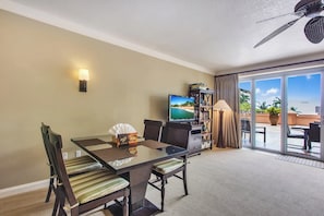 Une chambre d’hôtel équipée d’une table à manger en verre, de chaises, d’un téléviseur, d’une bibliothèque, d’une lampe et d’un ventilateur de plafond.