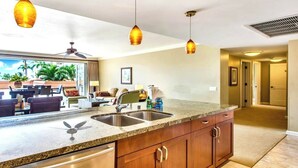 A kitchen with granite countertops, stainless steel sinks, wooden cabinets, and pendant lighting.