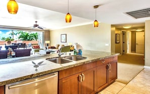 A kitchen with granite countertops, stainless steel sinks, wooden cabinets, and pendant lighting.
