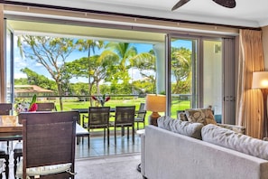 Un salon moderne doté d’une grande porte-fenêtre coulissante donnant sur un balcon avec vue sur un terrain de golf et une végétation luxuriante.