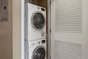 Une machine à laver Bosch est posée sur une autre machine à laver Bosch dans une buanderie avec une porte blanche et des stores.