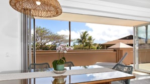 A dining area with a glass table, wicker chairs, and a hanging light fixture. - Honua Kai | Ocean View 5 BR, Sleeps 14 | Car Incl. w/ 6+ Nights | HKH ML-1634 by KBM (Lahaina)