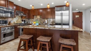 A modern kitchen with stainless steel appliances, granite countertops, and wooden bar stools.